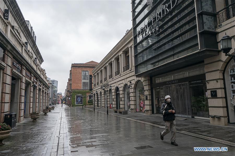 Seorang pria berjalan melintasi sebuah area di Wuhan yang terlihat sepi, Minggu (26/1/2020). Toko-toko terlihat tutup dan tak ada aktivitas.