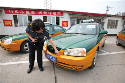 2014年7月4日,交通执法人员展示套牌出租车,与旁边的真出租车相比,套牌车左前方保险杠无字母数字编号。新京报记者 高玮 摄